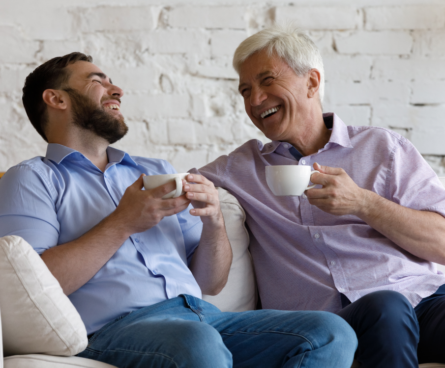 men sitting on couch, laughing and drinking coffee